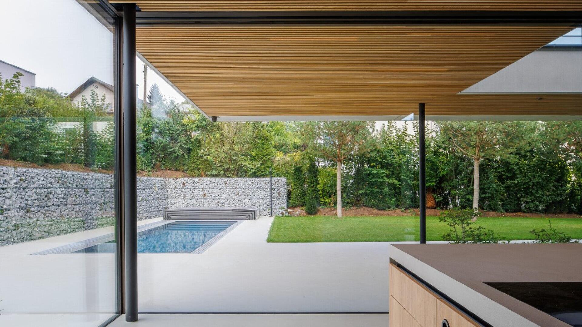 Maison moderne avec piscine, plafond en lattes de bois et jardin verdoyant.