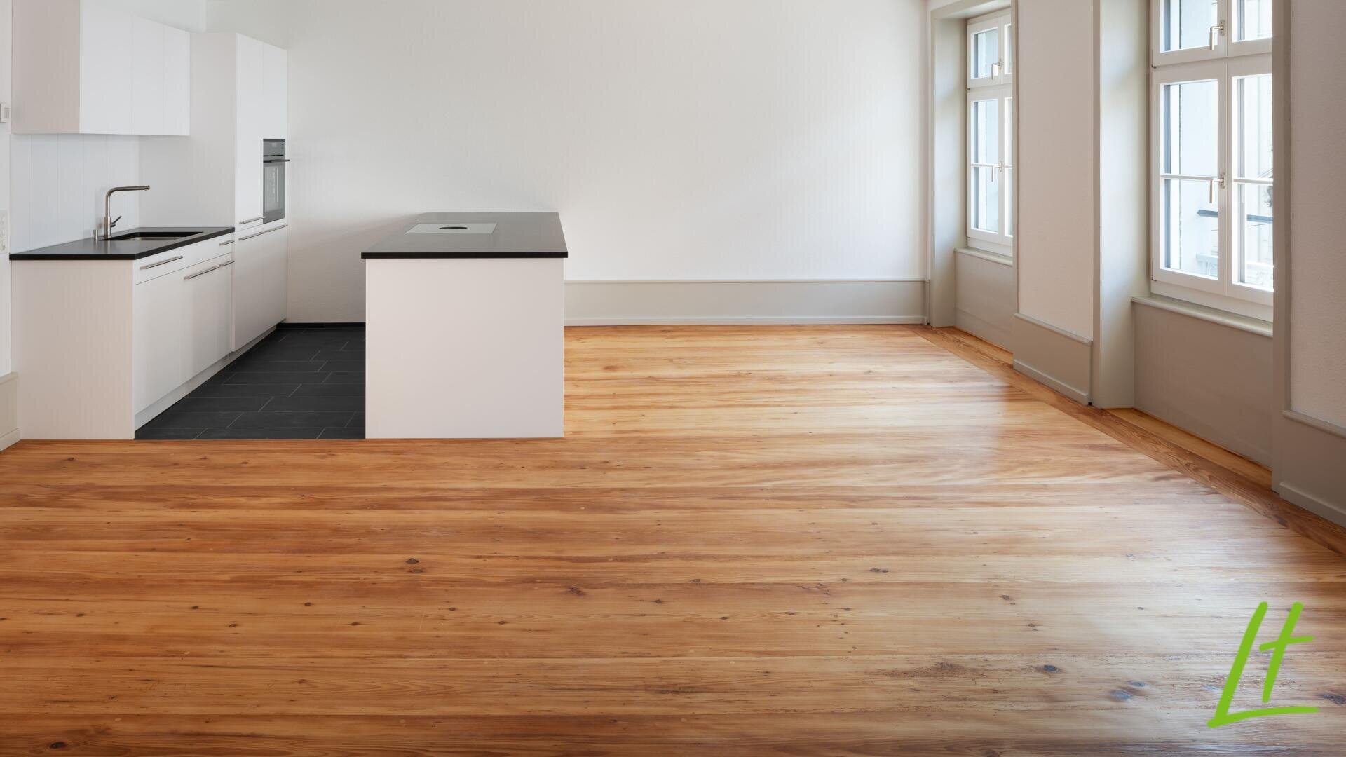 Appartement moderne, non meublé, comprenant une cuisine avec des armoires blanches, des plans de travail noirs, un îlot central et un espace de vie ouvert avec des sols en bois poli et de grandes fenêtres qui laissent entrer la lumière du jour.