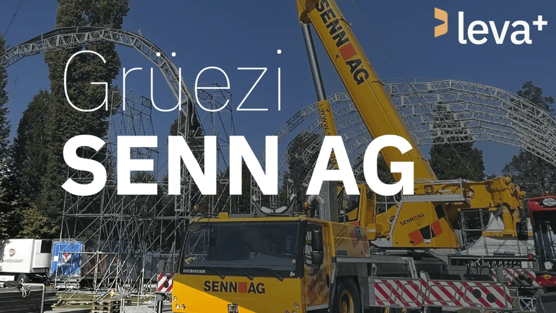 Ein gelber Kran der Senn AG arbeitet auf einer Baustelle mit Metallgerüsten im Hintergrund. In grosser weisser Schrift steht Grüezi SENN AG und in der rechten oberen Ecke erscheint das leva+ Logo.