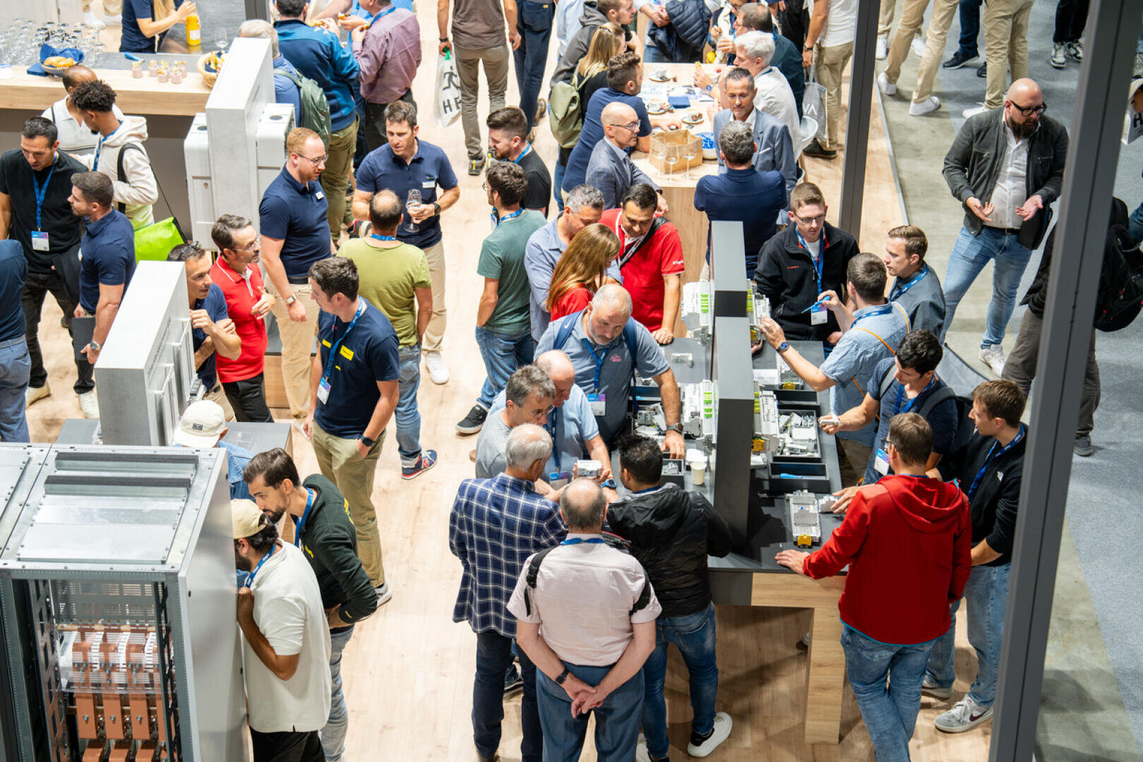 Auf einer gut besuchten Messe oder Konferenz versammelt sich eine große Gruppe von Menschen in einem Saal, unterhält sich und tauscht sich an verschiedenen Ausstellungsständen und Tischen aus.