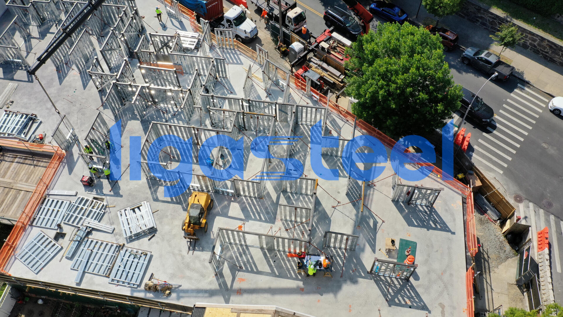 Luftaufnahme einer Baustelle mit Stahlgerüst, Arbeitern, Maschinen und Materialien. Auf einer nahe gelegenen Straße sind Autos geparkt, und ein grüner Baum ist zu sehen. Das Bild ist mit dem Wort figorsteel in blauer Schrift überlagert.