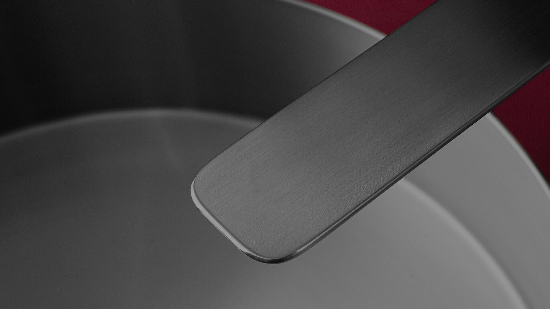 Nahaufnahme eines Edelstahltopfs mit passendem Metallgriff vor einem tiefroten Hintergrund. Das Innere des Topfes und der Griff sind aus gebürstetem Metall.