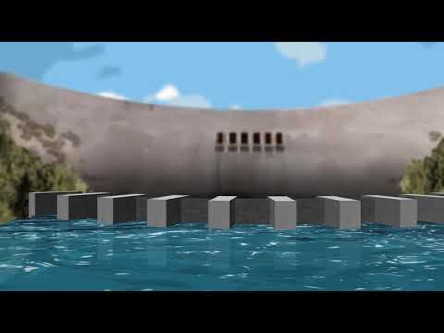 Im Hintergrund ist ein Damm mit mehreren rechteckigen Öffnungen zu sehen, während im Vordergrund unter einem blauen Himmel mit vereinzelten Wolken mehrere rechteckige Betonblöcke im Wasser liegen.