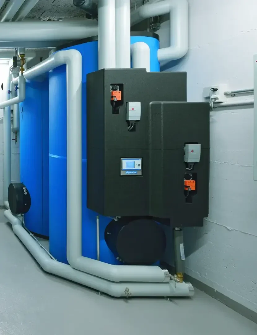 De grands réservoirs d'eau bleus sont reliés à des tuyaux isolés blancs et à des panneaux de commande noirs dans une salle de service ou une chaufferie propre et moderne, avec un sol gris et des murs peints en blanc.