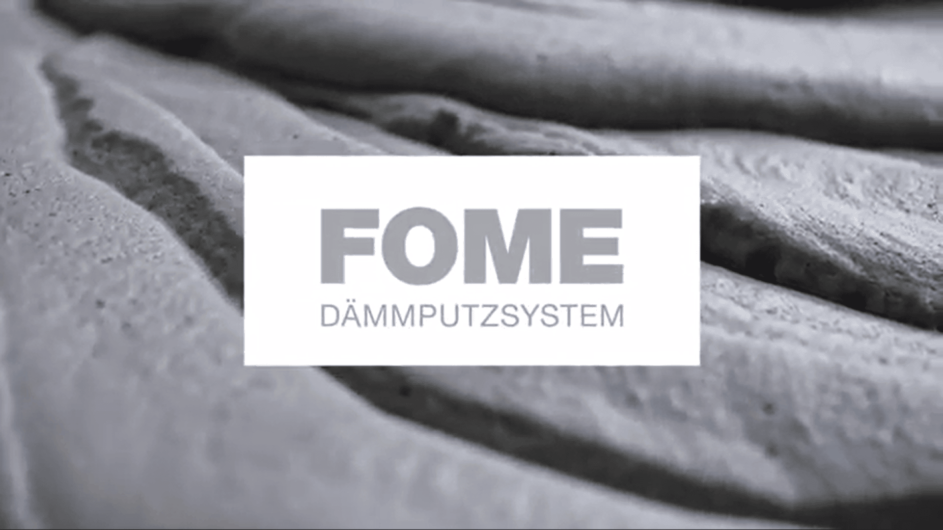 Nahaufnahme eines strukturierten, grauen Materials mit dem Schriftzug FOME DÄMMPUTZSYSTEM in fetten Buchstaben, zentriert auf einem weißen, rechteckigen Overlay.