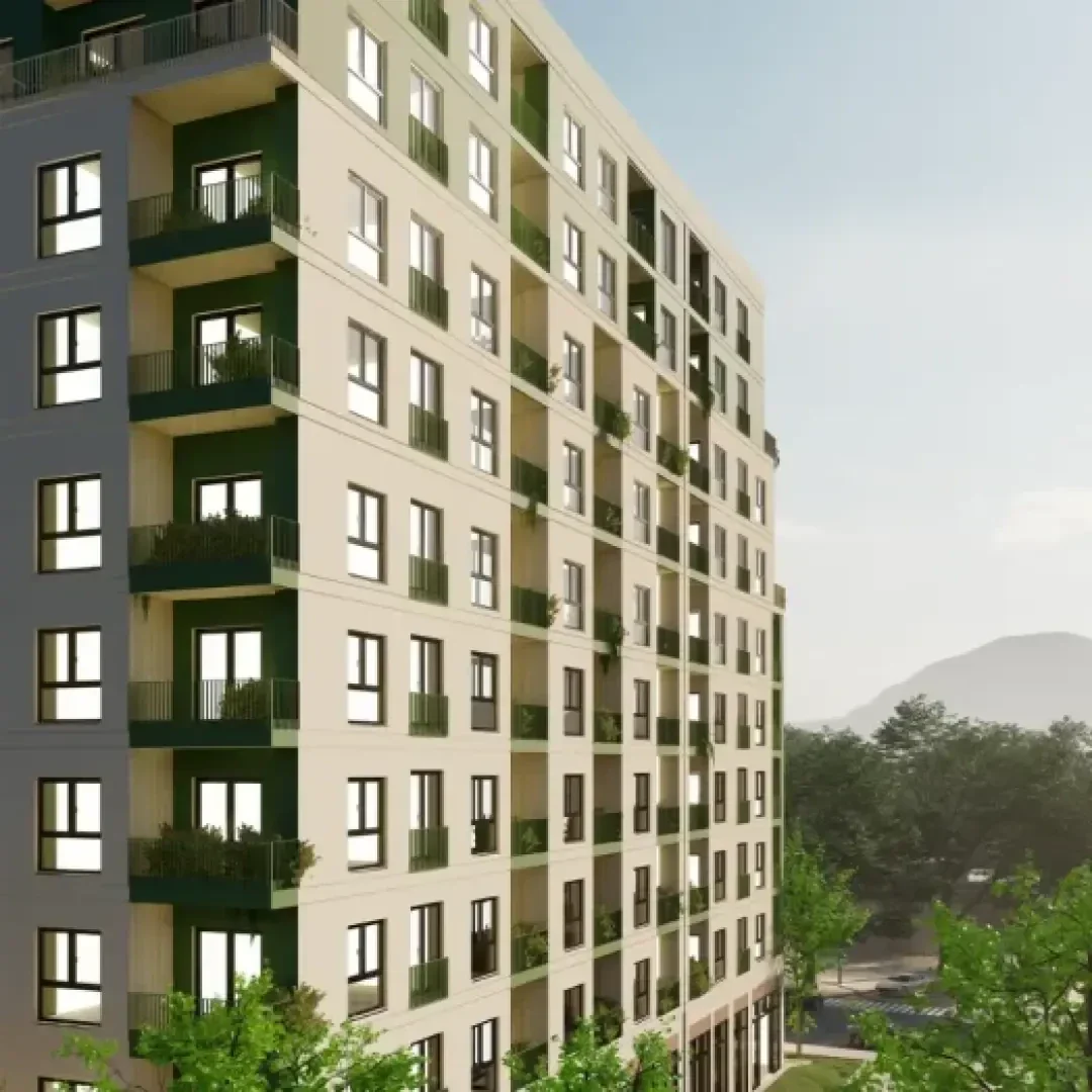 Ein modernes, mehrstöckiges Wohnhaus mit Balkonen und großen Fenstern, umgeben von grünen Bäumen. Der Himmel ist klar und im Hintergrund ist ein entfernter Hügel zu sehen.