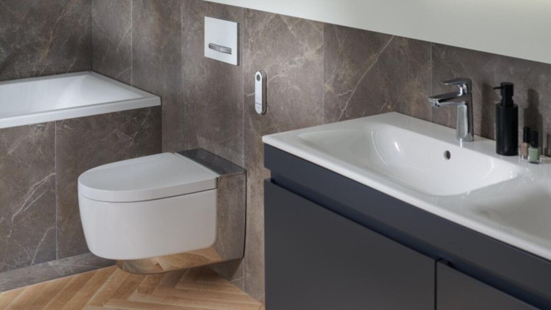 Une salle de bains moderne avec des toilettes murales, une baignoire, un lavabo élégant avec un meuble sombre et des murs en marbre. Des accessoires tels que des distributeurs de savon et des articles de toilette sont soigneusement disposés près du lavabo.