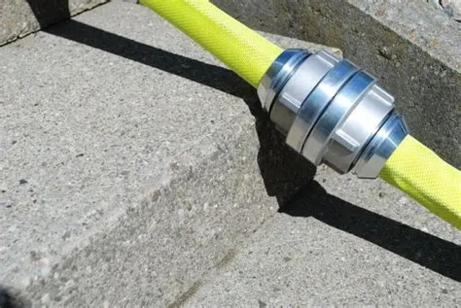 Ein leuchtend gelber Feuerwehrschlauch mit einer silbernen Metallkupplung liegt auf den Betonstufen im Sonnenlicht und wirft einen Schatten.