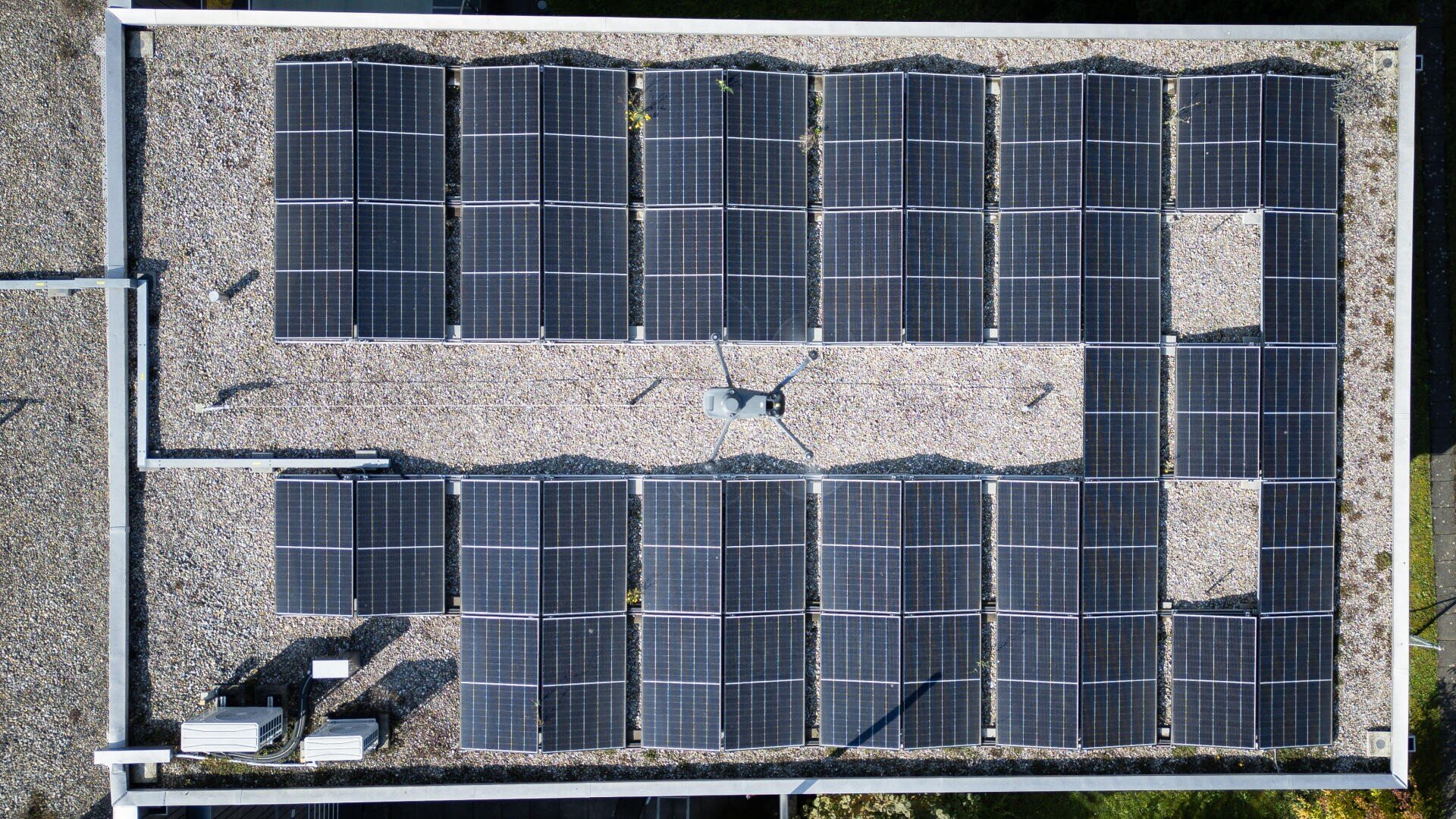 Luftaufnahme eines flachen Daches mit mehreren Reihen von Solarmodulen und Kies auf der Oberfläche, mit einigen Geräten und Kabeln in der Mitte der Module.