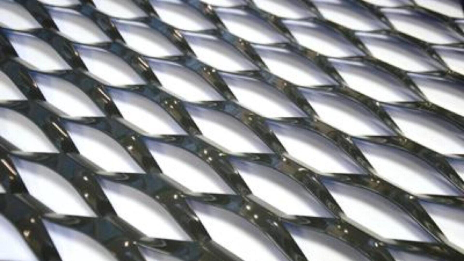 Gros plan d'une maille de métal déployé brillante et métallique, ornée de losanges, dont la surface réfléchit la lumière, créant un motif géométrique répétitif sur un fond blanc.