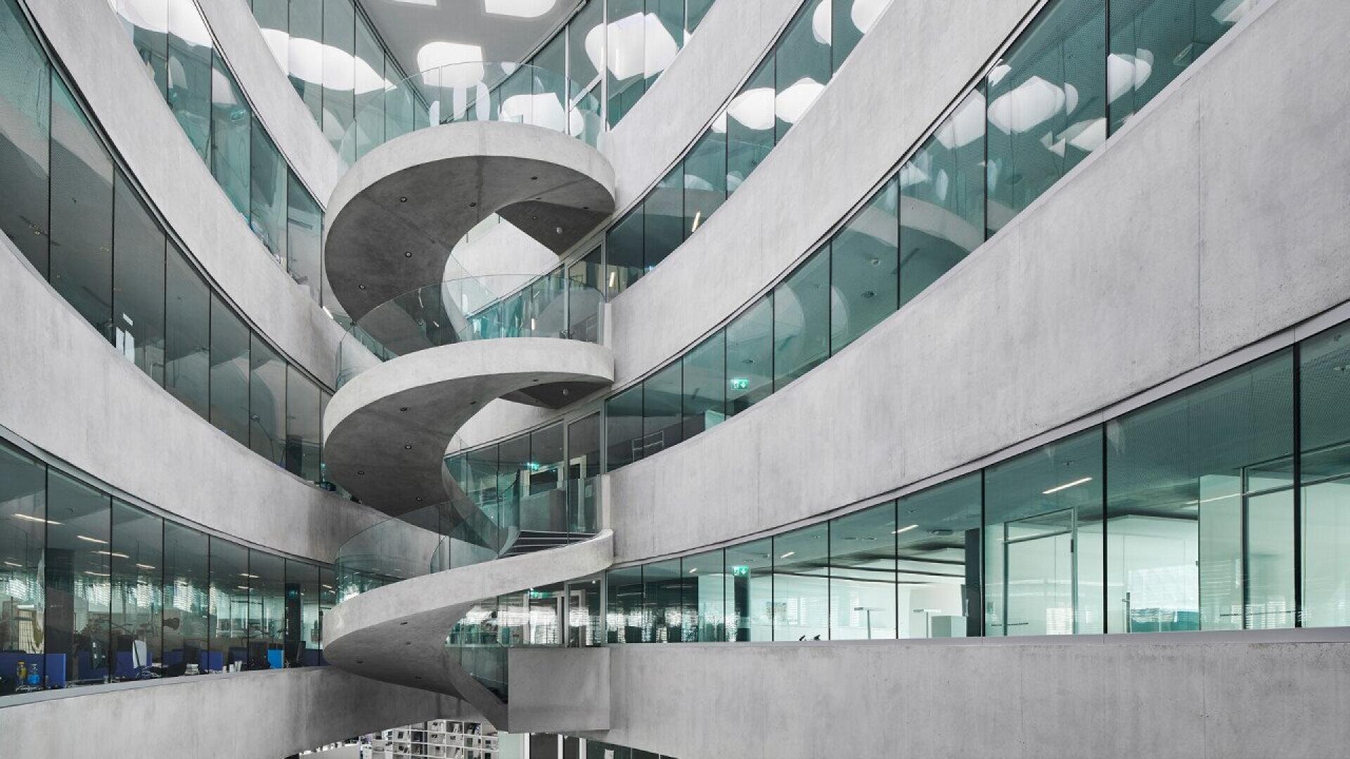 L'intérieur du bâtiment est moderne, avec des murs en béton incurvés, des bureaux vitrés et un large escalier en colimaçon reliant plusieurs étages, créant ainsi une atmosphère ouverte et aérée.