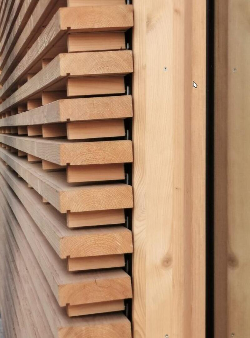 Nahaufnahme einer Holzwand mit horizontalen Latten auf der linken Seite, die ein sich wiederholendes Muster bilden, und einer flachen Holzplatte auf der rechten Seite. Das Holz erscheint glatt, hell und sauber verarbeitet.