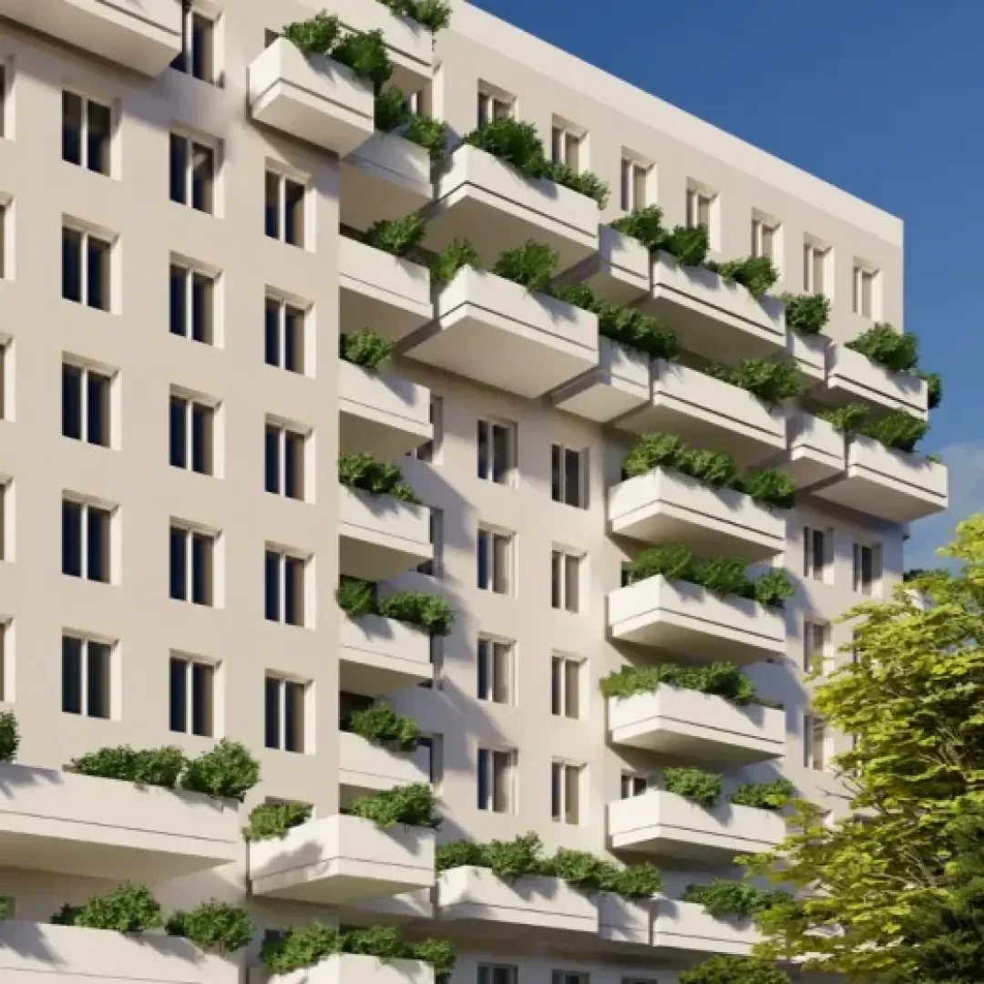 Un immeuble d'habitation moderne à plusieurs étages avec de nombreux balcons ornés de plantes vertes. La façade est peinte dans des couleurs claires et un arbre feuillu se trouve au premier plan.