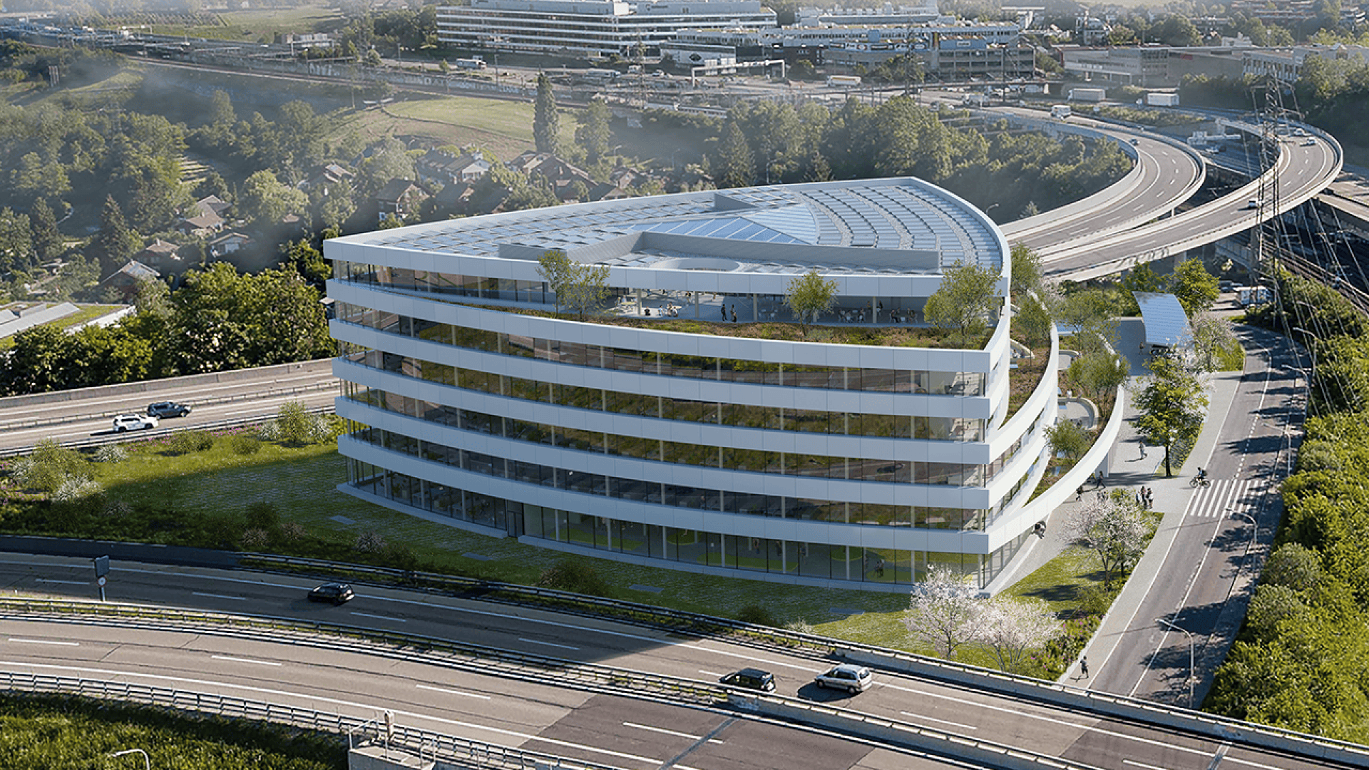 Un immeuble de bureaux moderne en verre incurvé, dont les terrasses sont recouvertes de verdure, est situé au bord de plusieurs autoroutes, entouré d'arbres et sur fond de bâtiments et de collines.