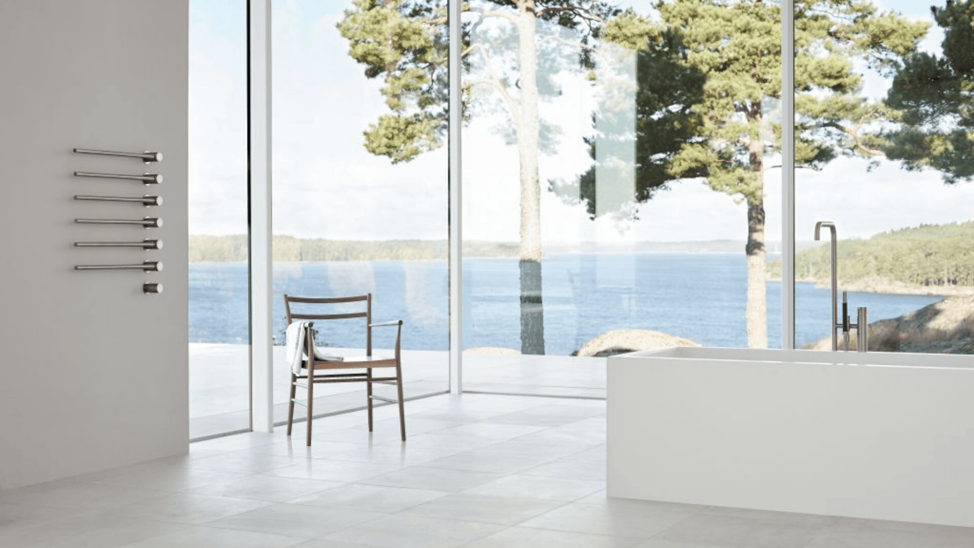 Ein modernes, minimalistisches Badezimmer mit großen, raumhohen Fenstern und Blick auf einen See und Bäume. Ein Holzstuhl, ein weißes Handtuch und eine weiße Badewanne sind in diesem hellen, luftigen Raum zu sehen.