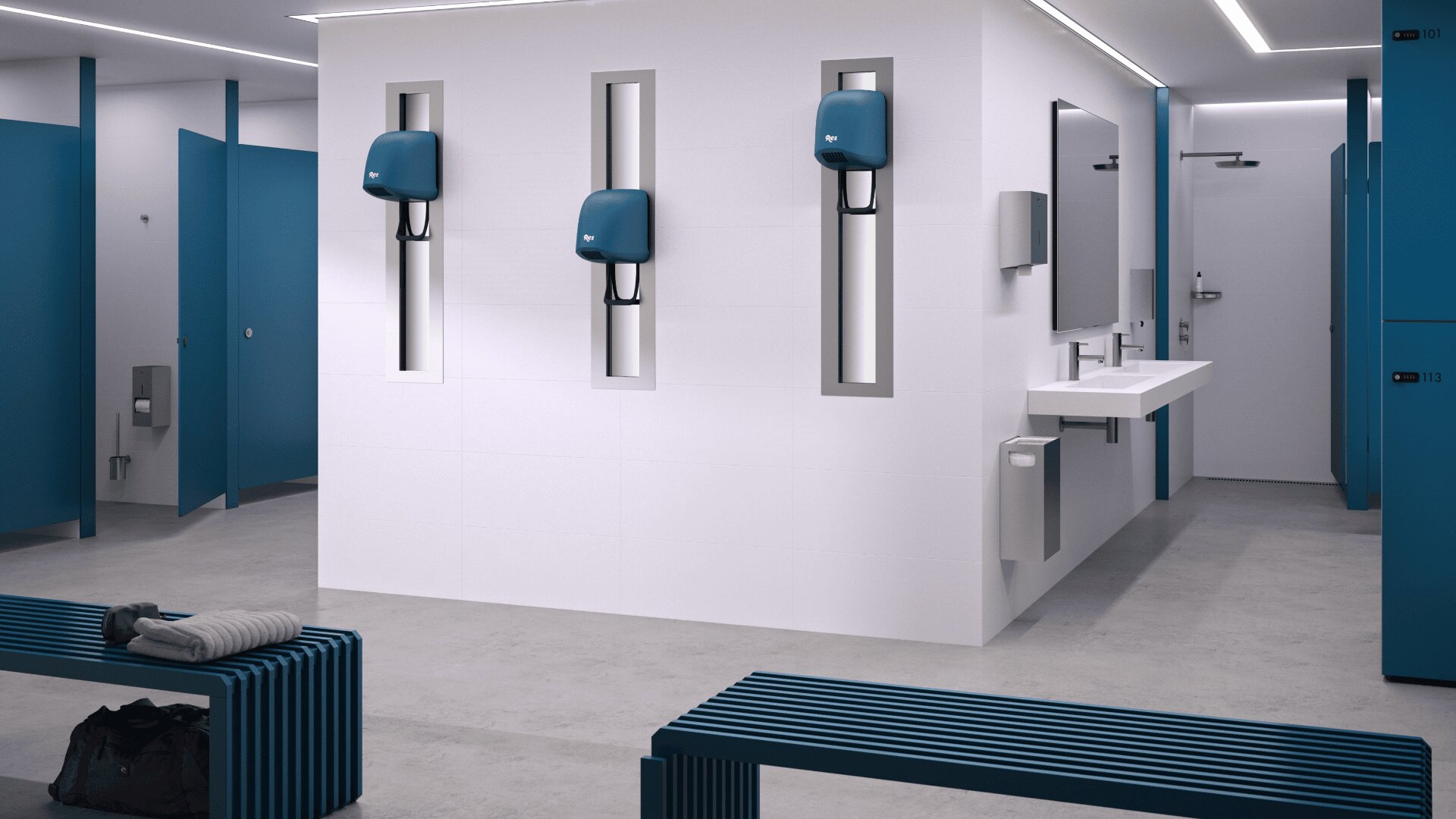 Vestiaire moderne avec des casiers et des bancs bleus et des murs blancs. Trois sèche-mains bleus et des lavabos sont installés sur un mur central. Une serviette et un sac de sport sont posés sur un banc au premier plan. L'endroit est propre et bien éclairé.