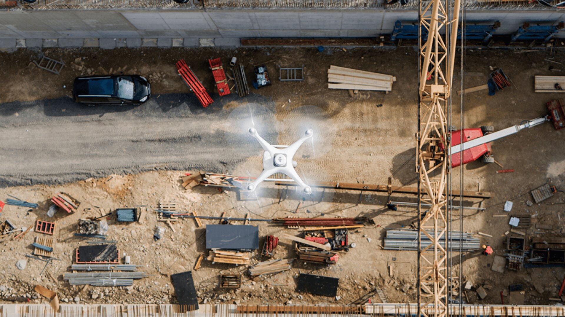 Luftaufnahme einer Baustelle mit einer Drohne, die über Trümmer, Holz und einen gelben Kran fliegt.