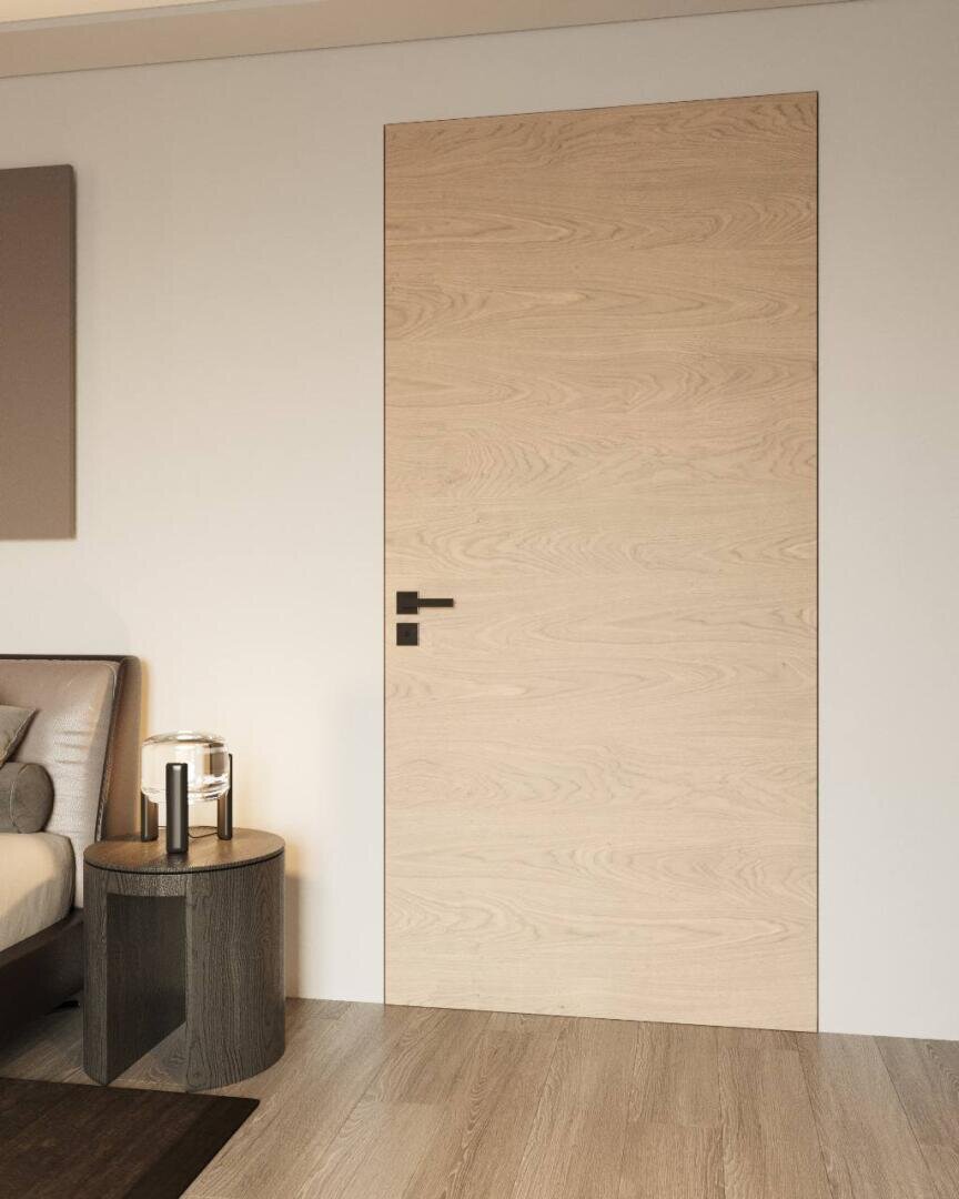 Ein modernes, minimalistisches Zimmer mit einer bündigen Tür aus hellem Holz, schwarzem Griff, hellem Holzboden, rundem Beistelltisch aus dunklem Holz mit schwarzem und gläsernem Dekor und einem Teil eines Bettes mit grauem Kopfteil.