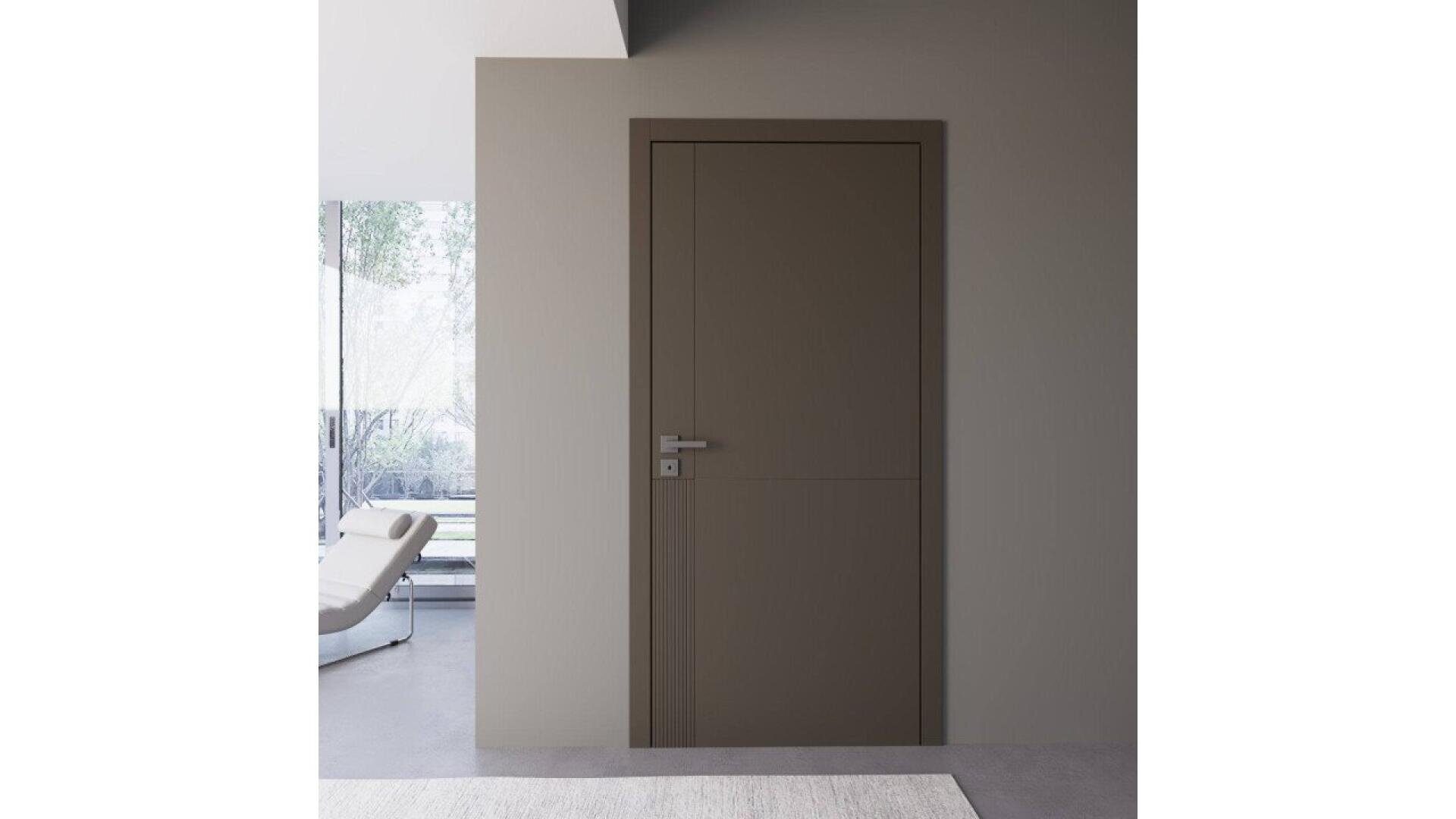 Une porte moderne en bois brun avec une poignée argentée est encastrée dans un mur gris clair. À gauche, une grande fenêtre avec vue sur les arbres et une chaise longue blanche. La pièce présente un design minimaliste.