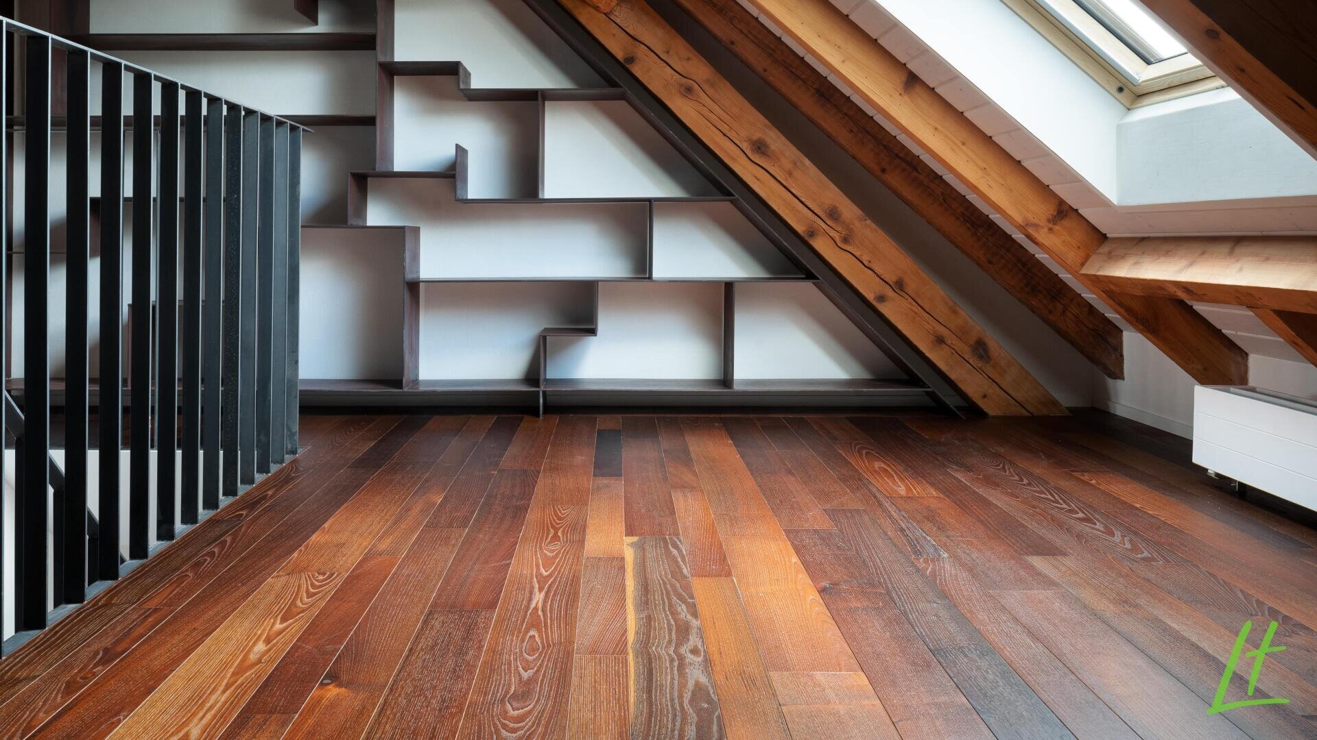 Ein modernes Dachgeschosszimmer mit schrägen Holzbalken, einem Oberlicht, dunklen Holzböden, einem einzigartigen geometrischen Bücherregal an der Wand und einem schwarzen Metallgeländer auf der linken Seite.