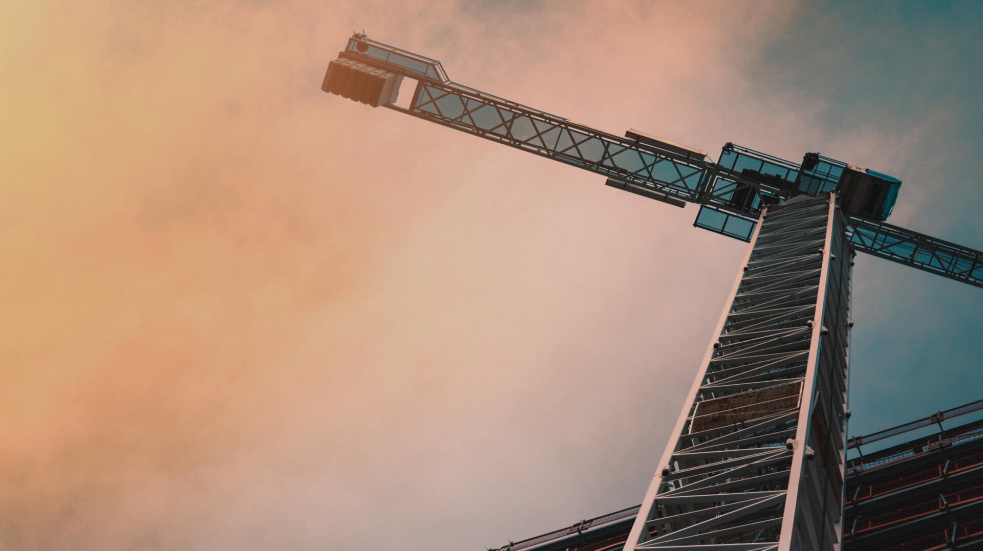 Ein Baukran wird von unten gegen einen Himmel mit einem Farbverlauf aus Orange- und Blautönen betrachtet, der die Metallstruktur und die Höhe des Krans betont.