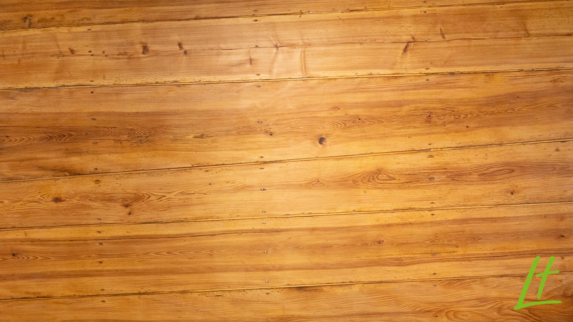 Des panneaux de bois à la surface chaude et naturelle et aux veines visibles s'étendent horizontalement sur le tableau. Dans le coin inférieur droit se trouve un petit "L" stylisé de couleur verte.