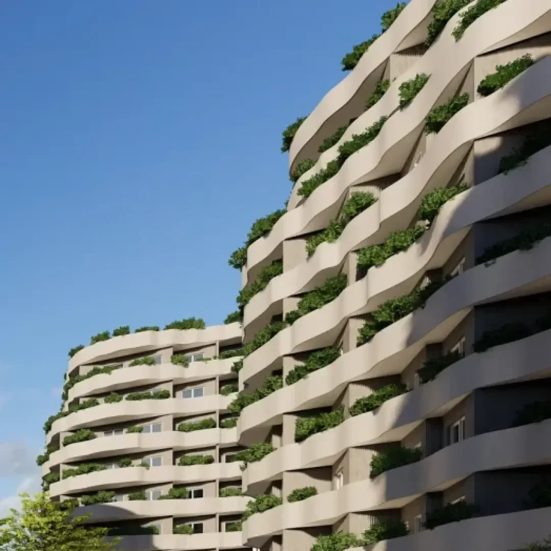 Des immeubles d'habitation modernes aux façades ondulées et beiges. Chaque balcon est recouvert de plantes vertes luxuriantes qui créent un effet de jardin vertical. Le ciel est clair et bleu, et on peut voir un arbre au premier plan.
