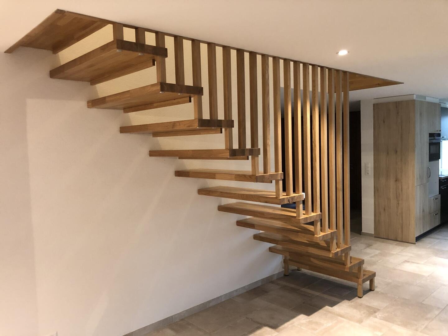 Un escalier flottant moderne en bois avec des contremarches ouvertes et des lattes verticales en guise de garde-corps, placé contre un mur blanc dans un espace intérieur contemporain.