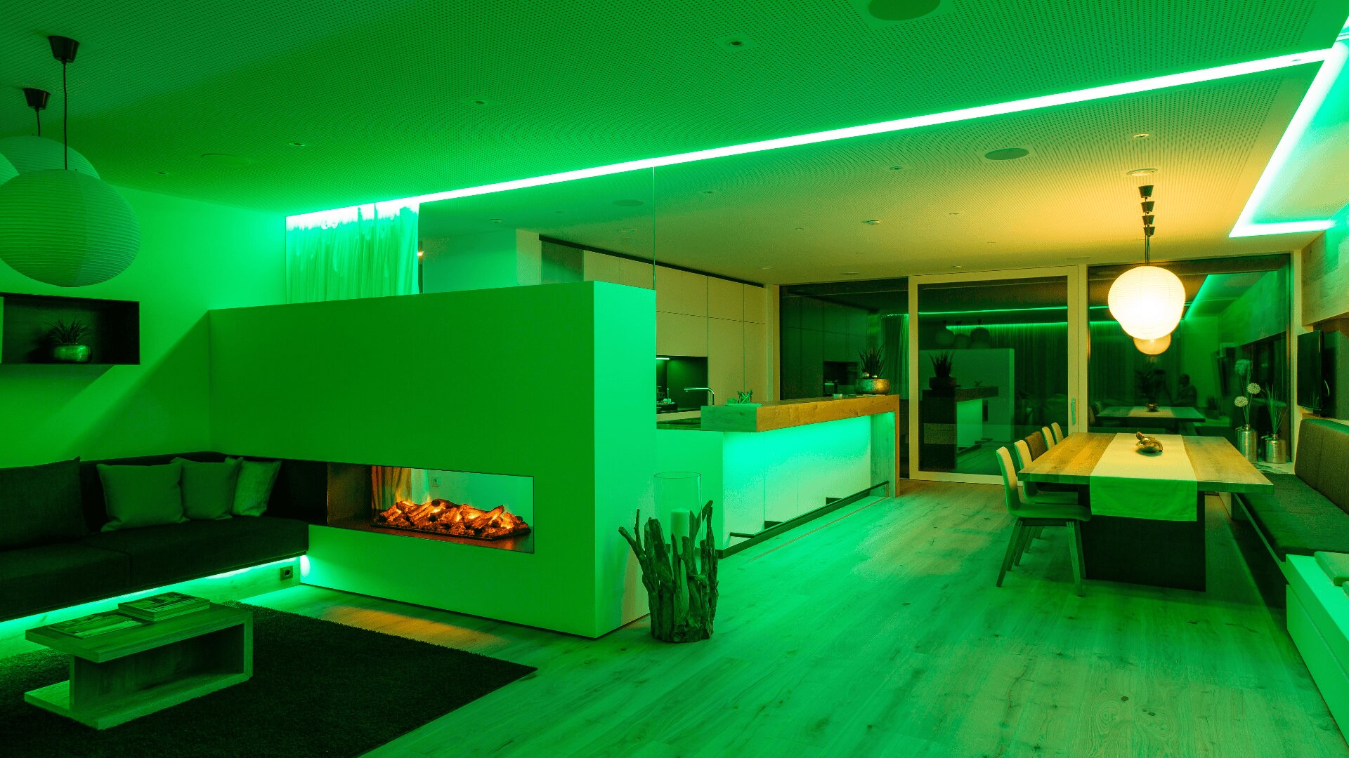 Moderner offener Wohn- und Essbereich mit grüner LED-Beleuchtung, eingebautem Kamin, Holzböden, großem Esstisch, Sofas und minimalistischem Dekor.