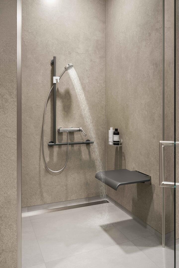 Douche accessible avec un siège fixé au mur, une douchette, des poignées et des étagères intégrées pour les articles de toilette ; design minimaliste avec des carreaux gris et une entrée ouverte et praticable.