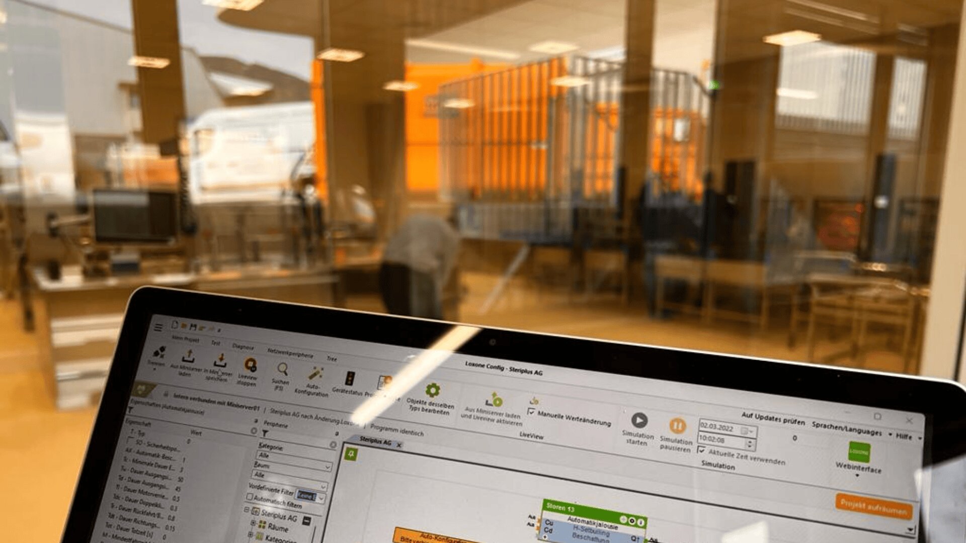 Ein Laptop-Bildschirm, auf dem eine Workflow-Software angezeigt wird, ist im Fokus, während ein Büro mit Schreibtischen, Computern und Menschen, die hinter Glaswänden arbeiten, im Hintergrund verschwommen erscheint.