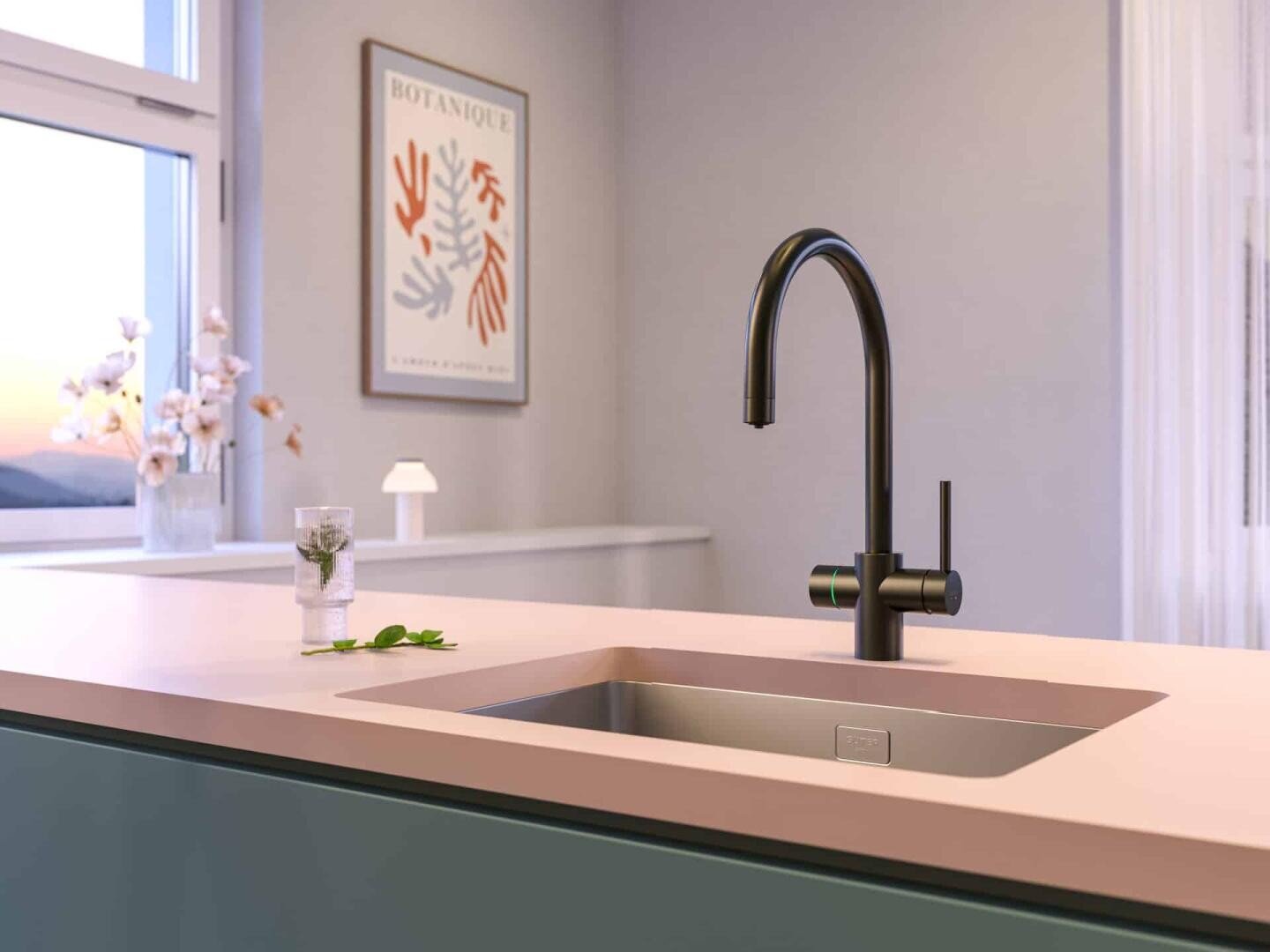 Cuisine moderne avec un robinet noir mat, un plan de travail rose et un lavabo en acier inoxydable. En arrière-plan, on peut voir un éclairage doux, une impression botanique encadrée et un vase avec des fleurs.
