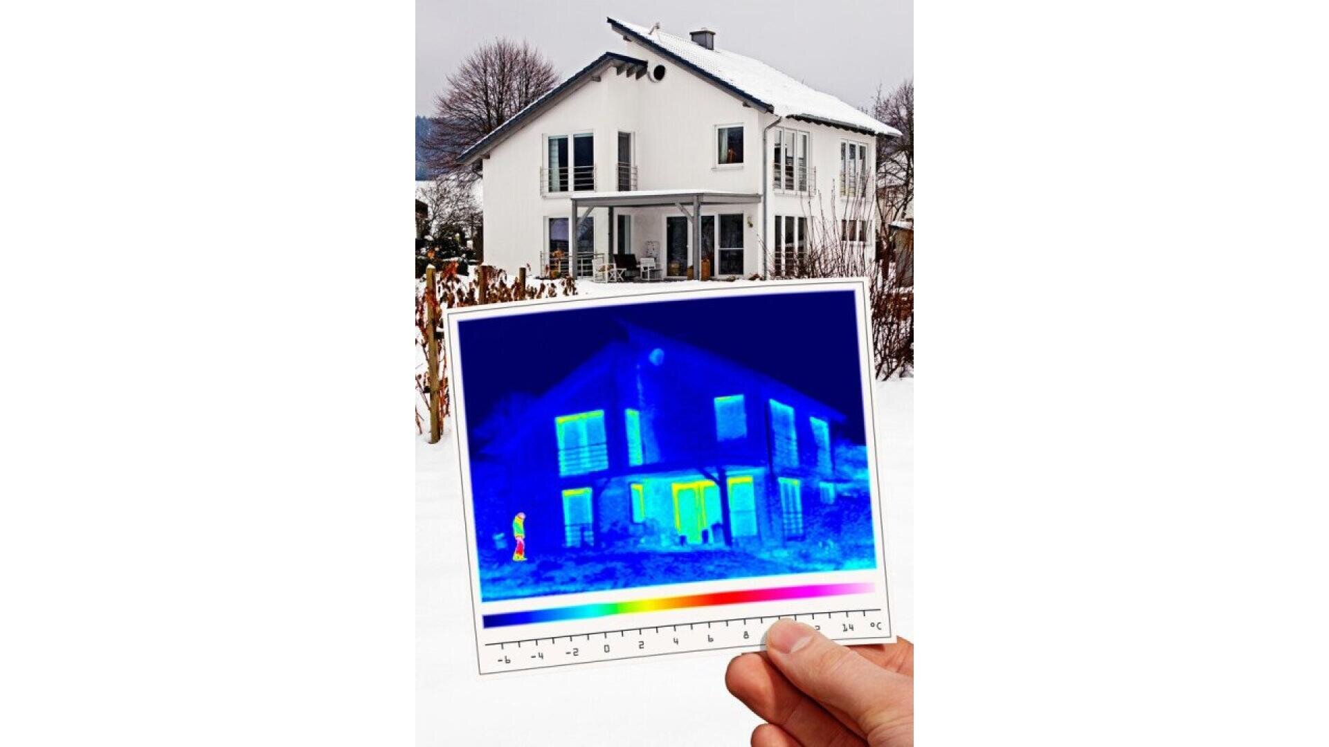 Une main tient une image thermique d'une maison devant la maison réelle par un jour de neige ; l'image thermique montre la perte de chaleur autour des fenêtres et des portes, alors que la maison réelle est recouverte de neige blanche.