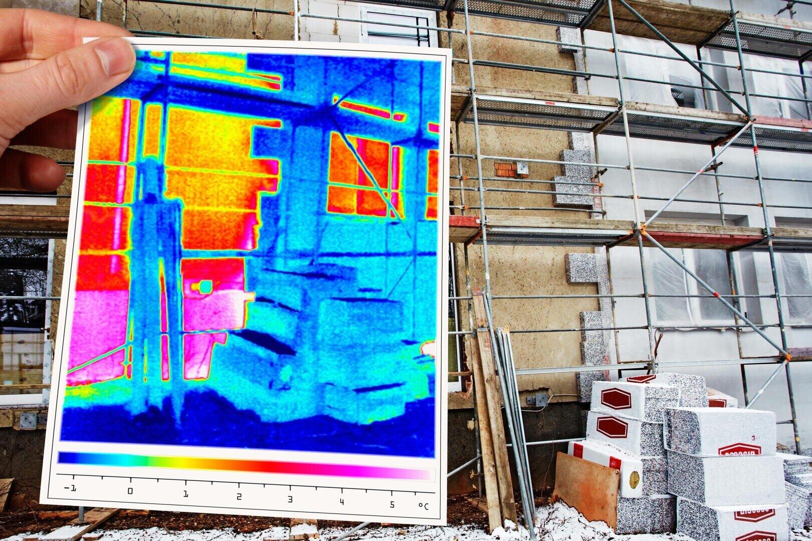 Une personne tient une image thermique devant un bâtiment en construction avec un échafaudage ; l'image thermique montre des zones de perte de chaleur en rouge et en jaune et des zones isolées en bleu. Des matériaux de construction sont empilés à proximité.