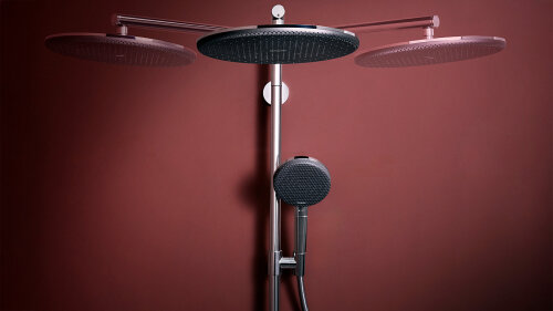 Une robinetterie de douche moderne avec trois grands pommeaux de douche ronds et un pommeau de douche à main devant un mur brun-rougeâtre.