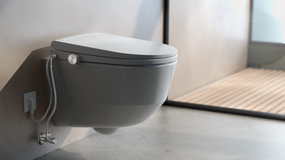 Un WC suspendu moderne à couvercle fermé, avec un élément de douche pour bidet et un décor de salle de bains minimaliste dans des tons neutres.