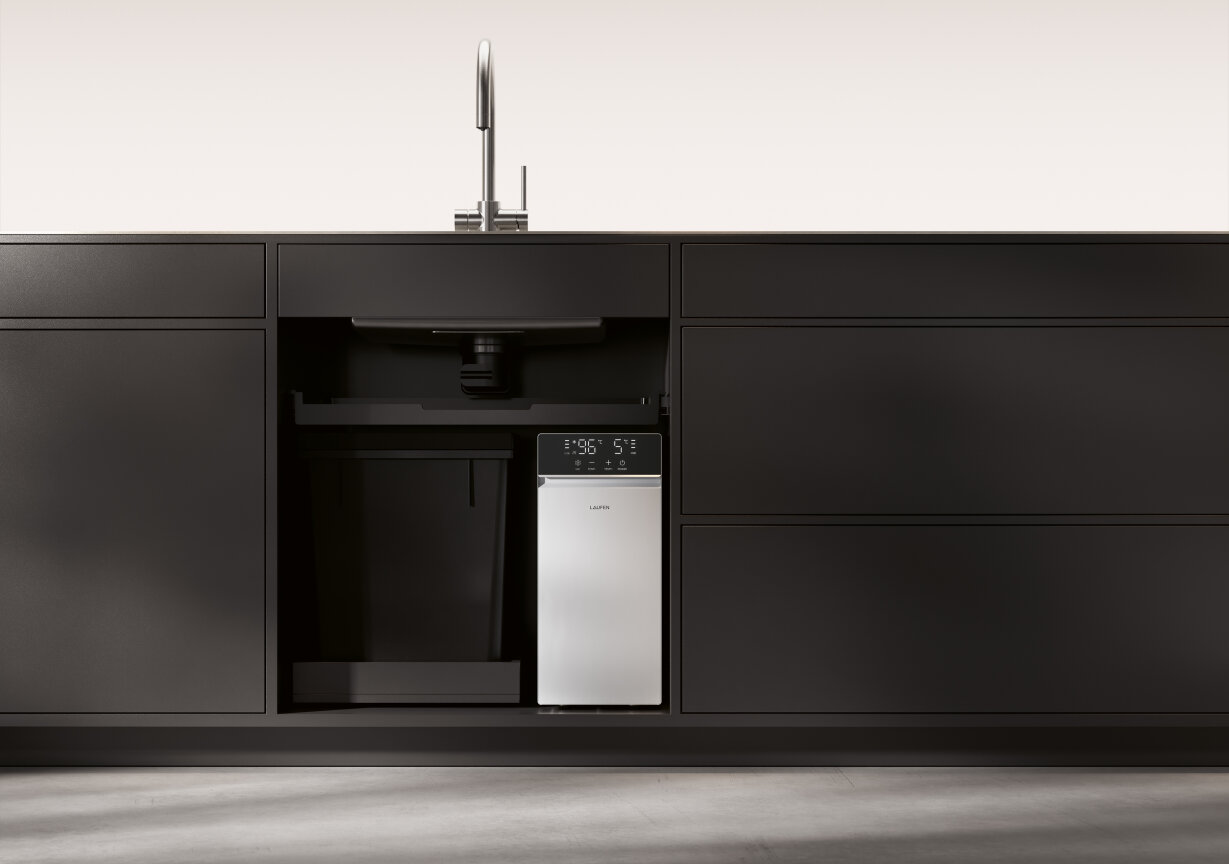 Eine moderne Küchenspüle mit schwarzen Schränken und einem kompakten Hightech-Gerät mit Digitalanzeige, das unter der Spüle installiert ist. Die umgebenden Schränke sind schlicht und minimalistisch.